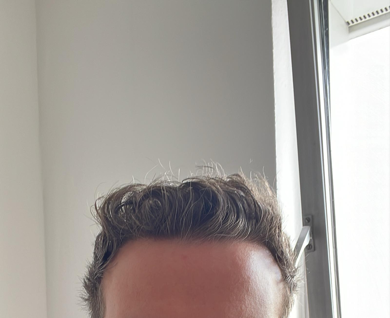 Obenansicht eines Mannes mit lockigem braunem Haar vor einem hellen Fenster