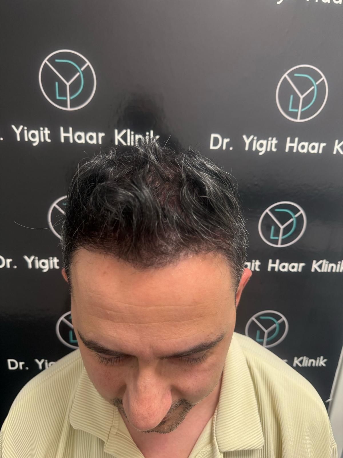 Ein Mann mit dunklem Haar blickt nach unten, im Hintergrund Kliniklogo auf schwarzer Wand