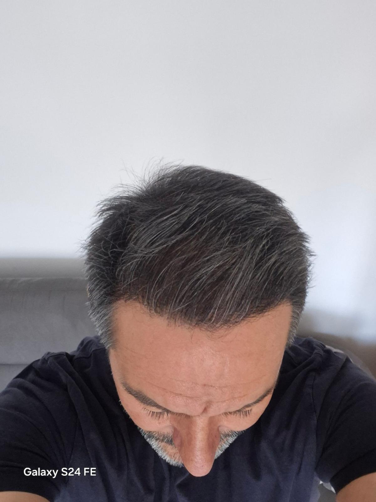 Ein Mann mit dunklem, leicht ergrautem Haar blickt nach unten und trägt ein schwarzes Shirt